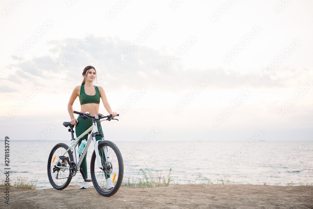 Beautiful young brunette woman resting after bicycle ride at sunrise. Model listening to music with wireless earbuds in the morning. Beautiful young brunette woman resting after bicycle ride at sunrise. Model listening to music with wireless earbuds in the morning.