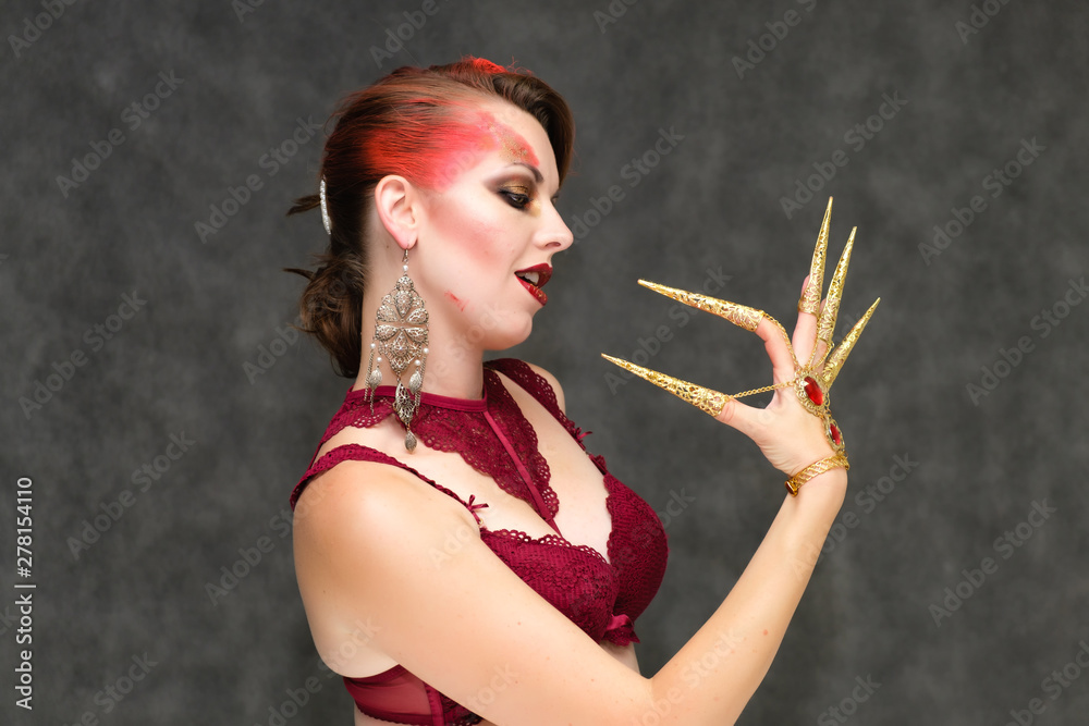 Obraz premium Portrait to the waist on a gray background of a pretty young brunette woman with beautiful makeup, with gold jewelry on her hand. Art, beauty, great makeup. Shows emotions.