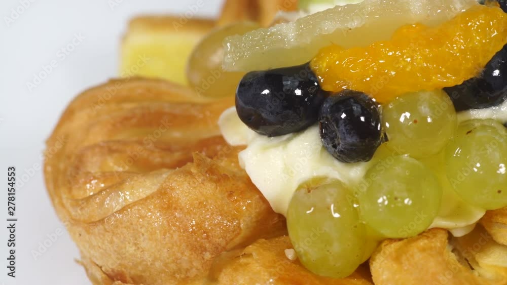 Close up puff pastry pie decorated with fresh blueberry and fruit slices - kiwi, grapes, ananas. Cake rotating