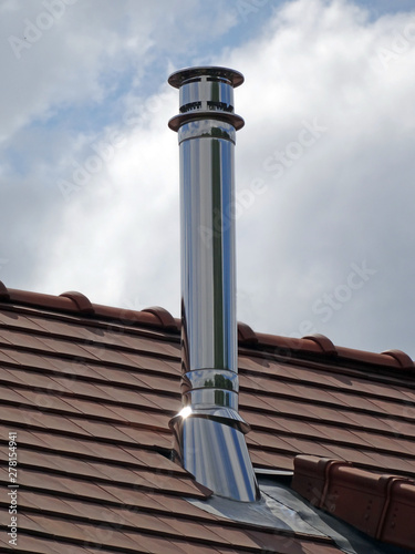 One metallic - iron stell material - chimney pipe with metal reflection on a red modern tiles roof against sky photo