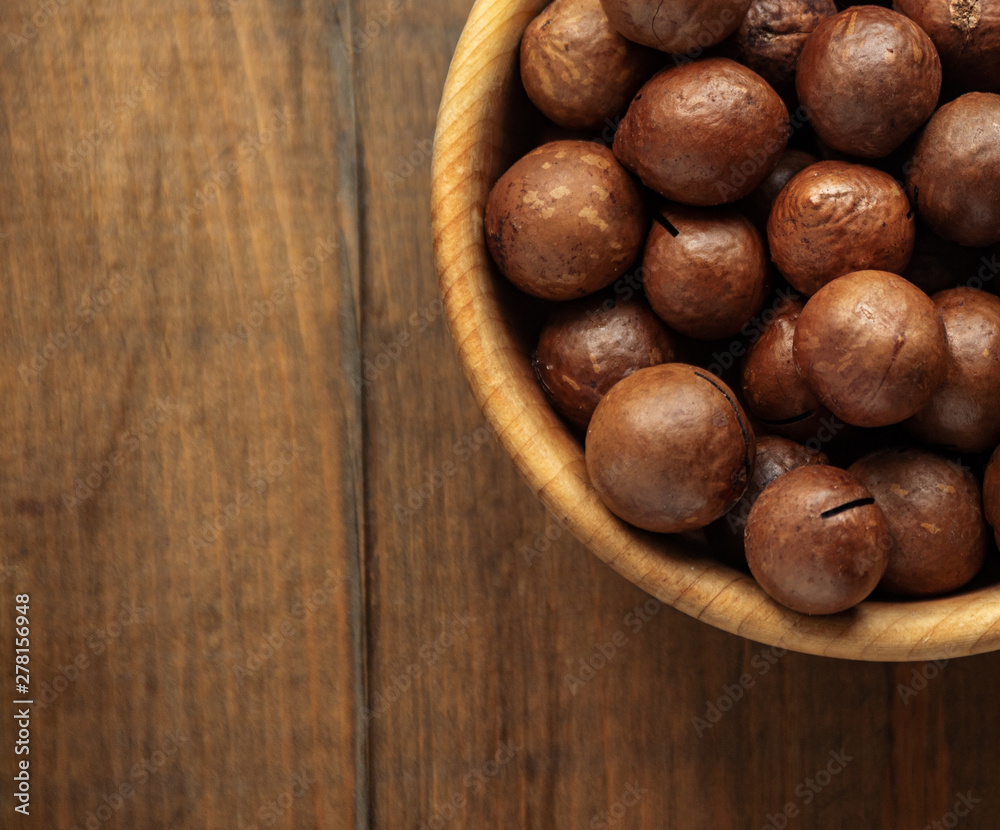 Macadamia nuts piled up in a wooden bowl and stand on a table with free space for text Macadamia nuts piled up in a wooden bowl and stand on a table with free space for text