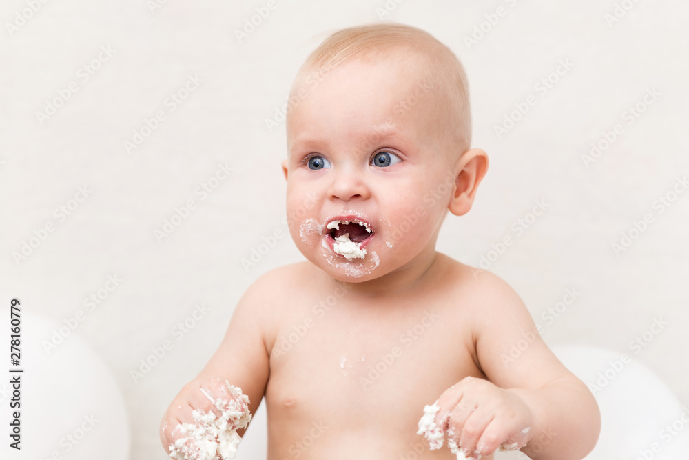 Baby birthday party. Infant eating birthday cake. Hungry boy on a light background with white ballons and copy space smash the cake Baby birthday party. Infant eating birthday cake. Hungry boy on a light background with white ballons and copy space smash the cake