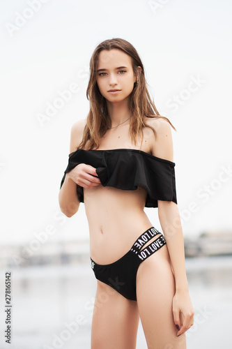 Beautiful tanned girl model in black swimwear with sexy body standing on beach. Summer vacation. Concept of sporty model, swimwear.