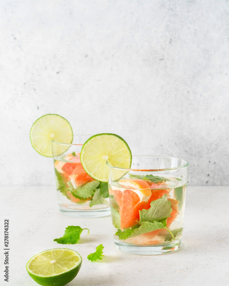 Fototapeta premium Glass of cool infused water with fresh grapefruit, lime and mint, (lemonade, cocktail). Detox drink, health care, fitness, diet concept.