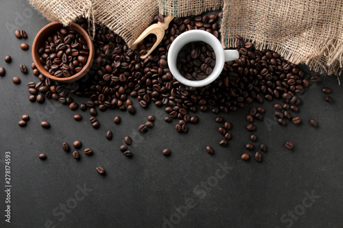 Roasted coffee beans in a cup and wooden spoon on a black background. Robusta, Arabica. top view.