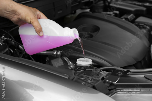 Man pouring liquid from plastic canister into car washer fluid reservoir, closeup