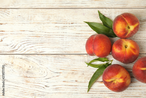 Fresh peaches and leaves on white wooden table, top view with space for text photo