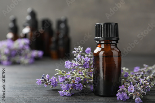 Bottle with natural lavender oil and flowers on wooden table against grey background, closeup view. Space for text