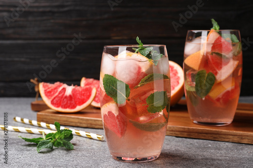 Glass of refreshing drink with grapefruit and mint on grey stone table against dark background, space for text