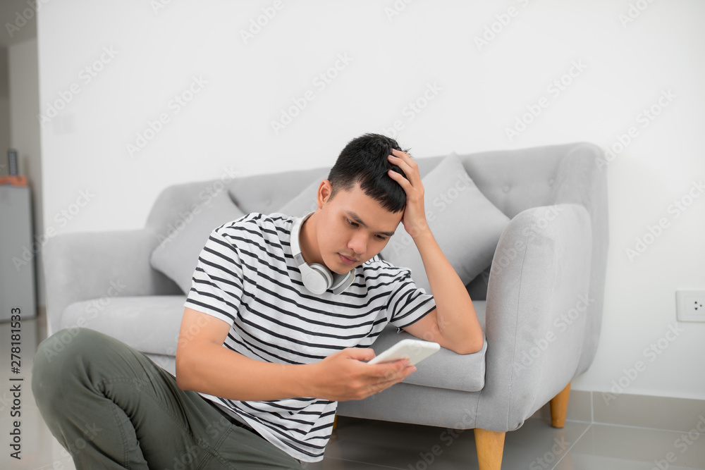 Single sad man checking mobile phone sitting on the floor in the living room at home