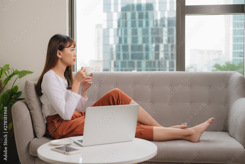 Young woman in casual clothes sitting on sofa at cozy home interior. Technology and communication concept. Young woman in casual clothes sitting on sofa at cozy home interior. Technology and communication concept.