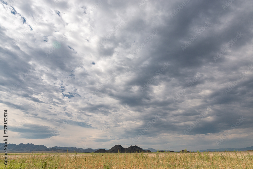 panoramic view of plain at root of mountains with white fluffy clouds in blue sky panoramic view of plain at root of mountains with white fluffy clouds in blue sky
