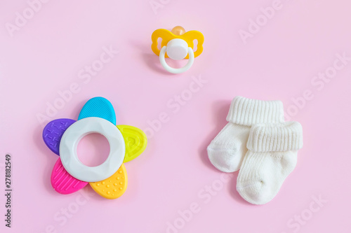 Baby accessories for newborns: socks, toy and  soother on pink background. Motherhood concept. Top view, flat lay composition. 