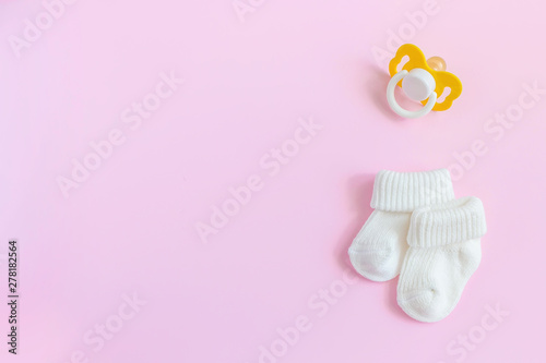 Baby accessories for newborns: socks and soother on pink background. Motherhood concept. Top view, flat lay composition. Copy space for text. photo