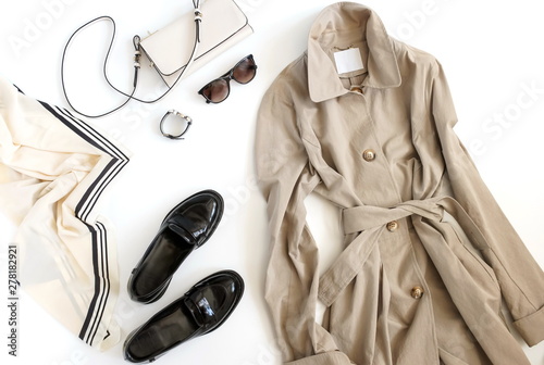 Women fashion clothes and accessories top view background. Flat lay female autumn style look with  beige trench, cloak , shoes, bag, sunglasses, accessories on white background. Copy space.