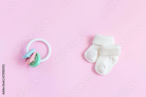 Baby accessories for newborns: socks and toy on pink background. Motherhood concept. Top view, flat lay composition.