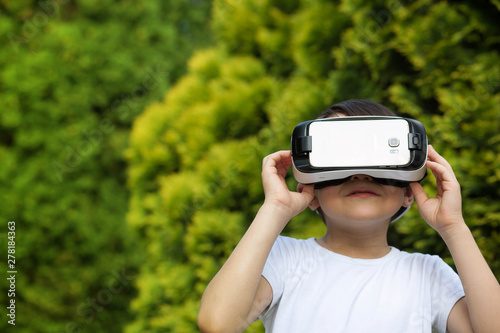 Cute little boy using VR glasses outdoors in a park - Blogger testing augmented reality goggles concept - Gamer exulting during 3D video game playing photo