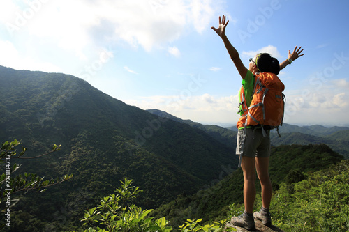Cheering young woman backpacker enjoy the view at summer mountain peak