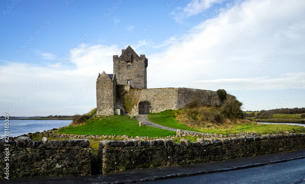 Ruins of old Dunguaire Castle with green grass, stream and lake, Ireland