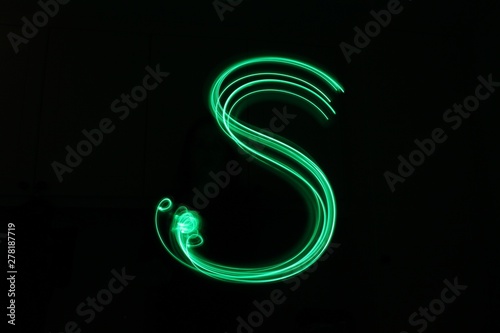 Long exposure photograph, light painting photography. Letter s of an alphabet series, single letter, in neon green light, against a black background
