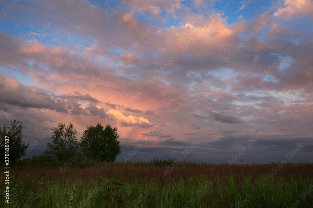 Beautiful thunderstorm clouds at sunset over the summer field.
