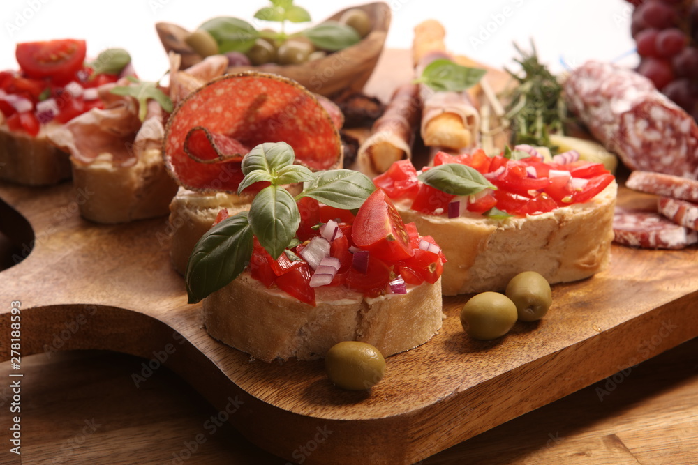 Traditional italian antipasto bruschetta appetizer with cherry tomatoes, cream cheese, basil leaves and balsamic vinegar on cutting board with prosciutto, salami, cheese Traditional italian antipasto bruschetta appetizer with cherry tomatoes, cream cheese, basil leaves and balsamic vinegar on cutting board with prosciutto, salami, cheese