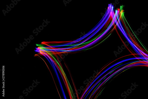 Long exposure photograph of neon multi colour in an abstract swirl parallel lines pattern against a black background. Light painting photography.