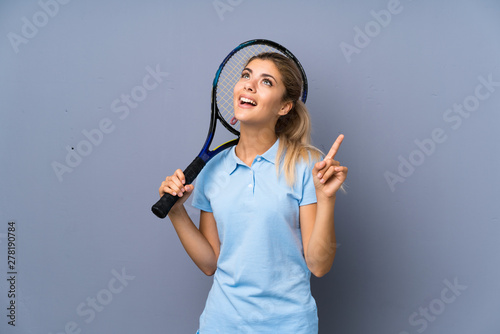 Teenager tennis player girl over grey wall intending to realizes the solution while lifting a finger up