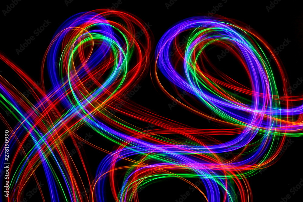 Long exposure photograph of neon multi colour in an abstract swirl parallel lines pattern against a black background. Light painting photography.