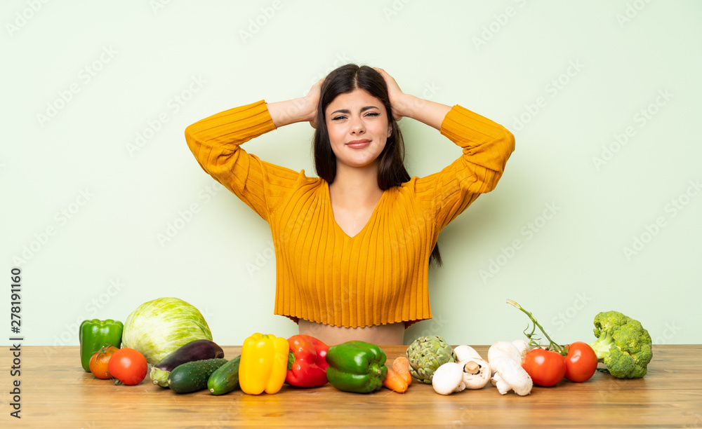 Fototapeta premium Teenager girl with many vegetables frustrated and takes hands on head