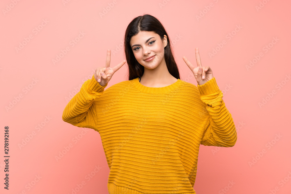 Teenager girl over isolated pink wall showing victory sign with both hands Teenager girl over isolated pink wall showing victory sign with both hands
