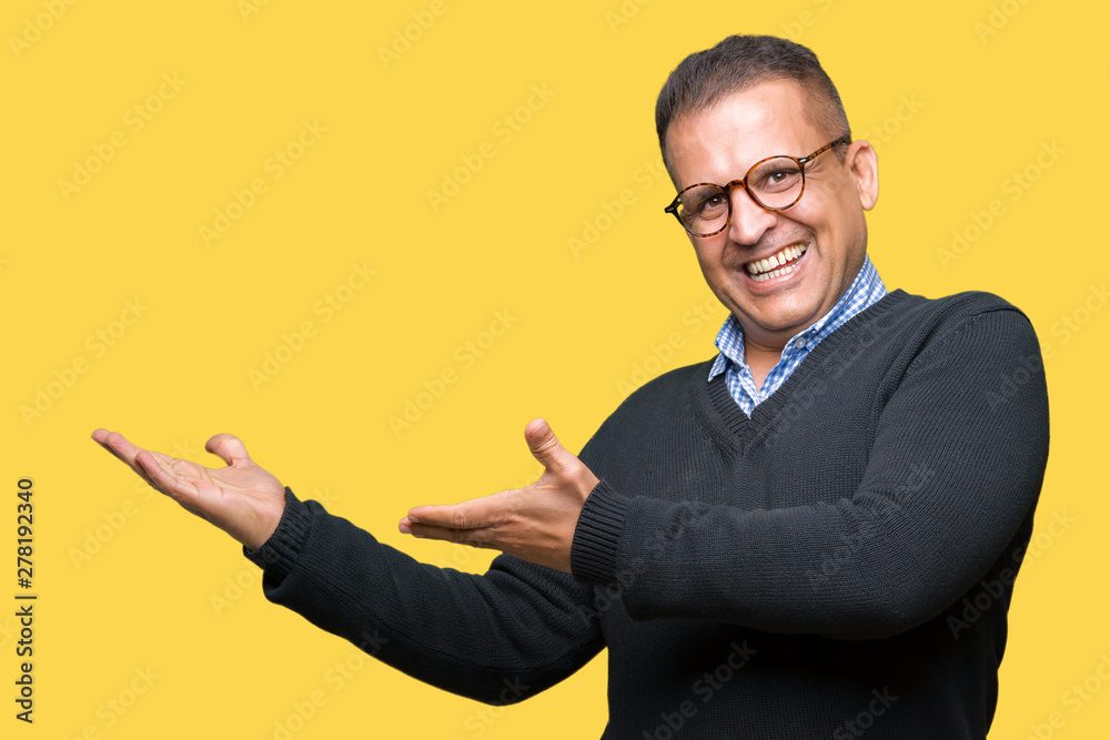 Middle age bussines arab man wearing glasses over isolated background amazed and smiling to the camera while presenting with hand and pointing with finger. Middle age bussines arab man wearing glasses over isolated background amazed and smiling to the camera while presenting with hand and pointing with finger.
