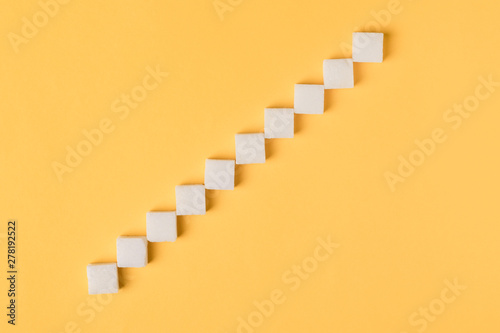 Ladder from sugar cubes over orange background