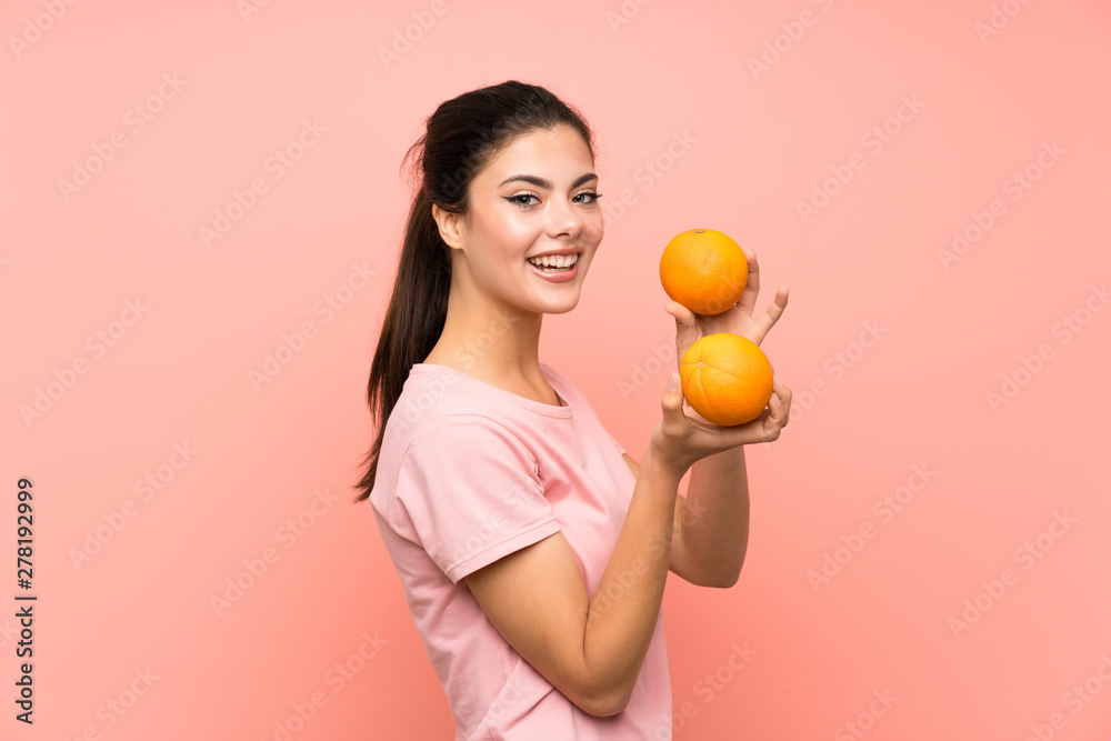 Happy Teenager girl over isolated pink wall holding oranges Happy Teenager girl over isolated pink wall holding oranges