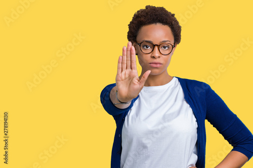 Young beautiful african american woman wearing glasses over isolated background doing stop sing with palm of the hand. Warning expression with negative and serious gesture on the face.