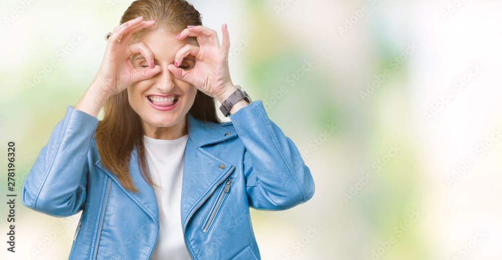 Beautiful middle age mature woman wearing fashion leather jacket over isolated background doing ok gesture like binoculars sticking tongue out, eyes looking through fingers. Crazy expression.