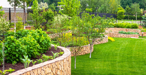 Landscaping in home garden. Beautiful natural landscape design with flower beds in summer. Panoramic view of landscaped part with plants in yard or backyard of residential house.