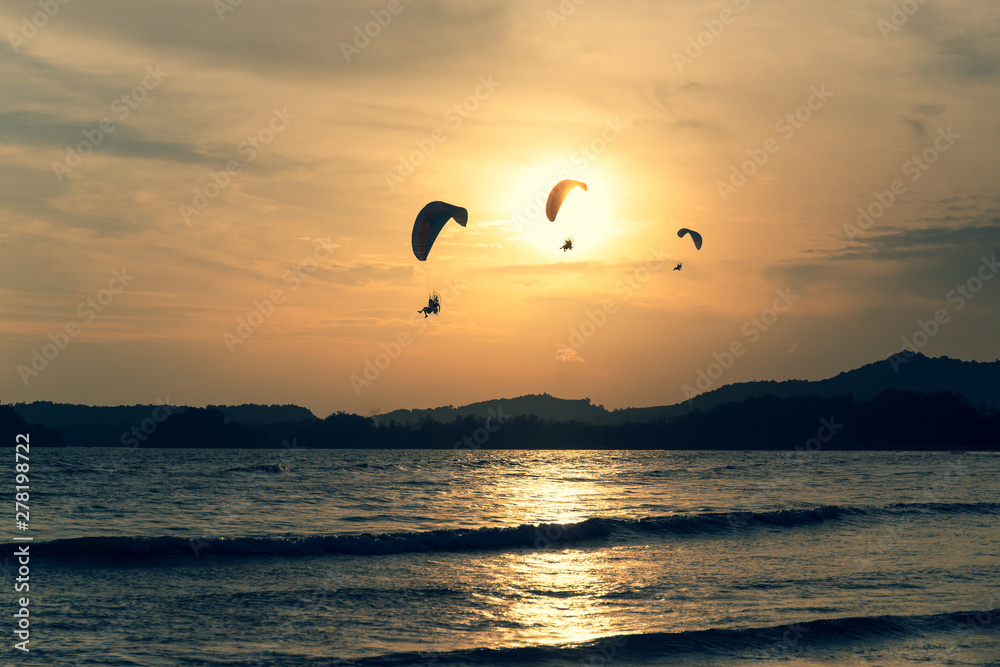 Beautiful Silhouette of paraglider flying in the sky of sunset on the beach.