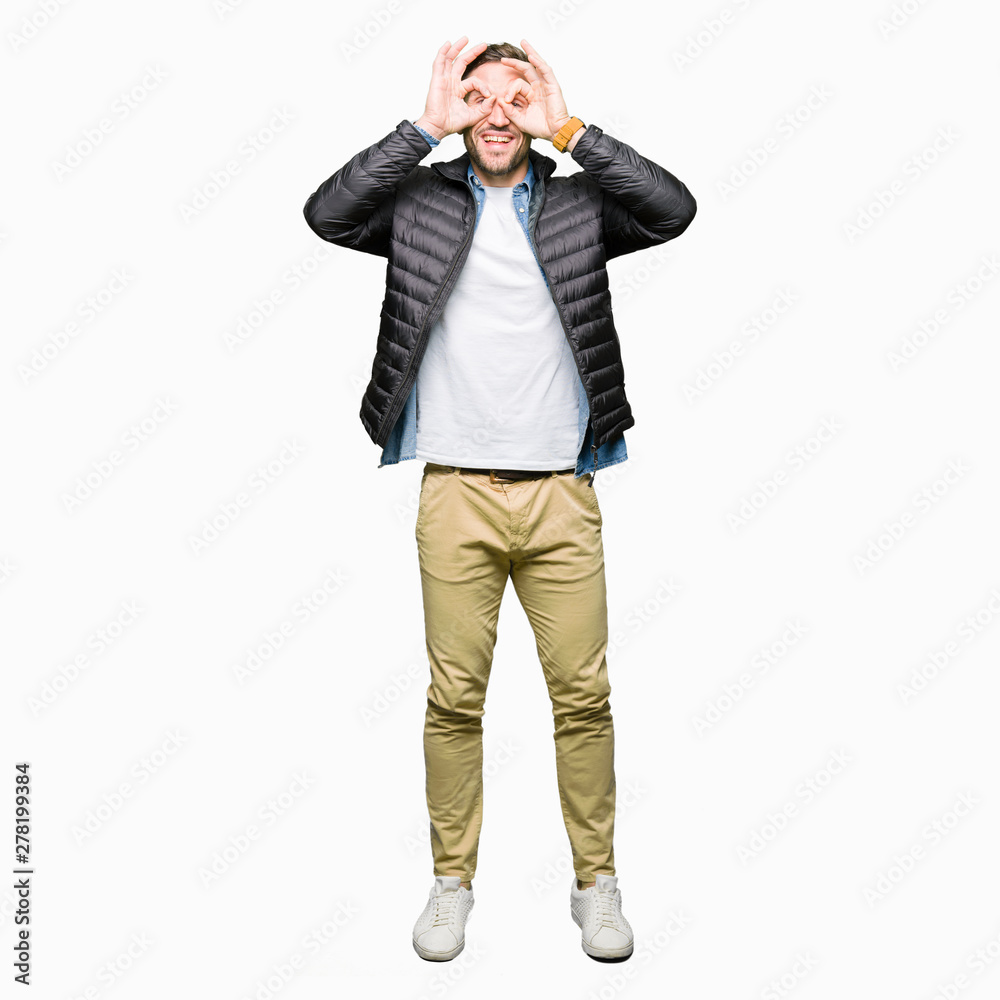 Handsome man wearing winter coat doing ok gesture like binoculars sticking tongue out, eyes looking through fingers. Crazy expression. Handsome man wearing winter coat doing ok gesture like binoculars sticking tongue out, eyes looking through fingers. Crazy expression.