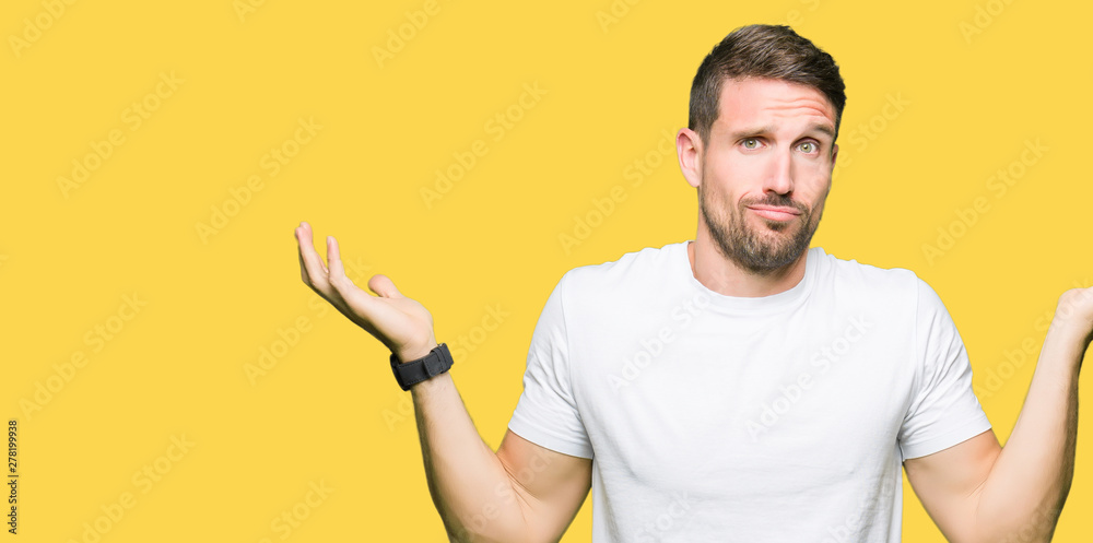 Handsome man wearing casual white t-shirt clueless and confused expression with arms and hands raised. Doubt concept.