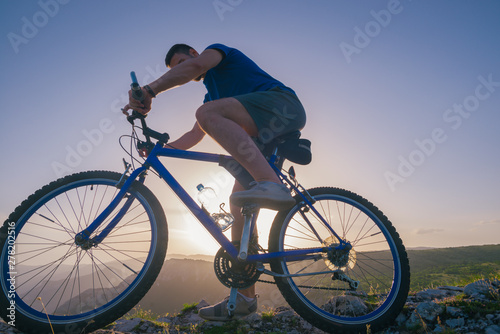 Fototapeta Naklejka Na Ścianę i Meble -  Strong fit male mountain biker performing stunts on rocky terrain on a sunset while wearing a blue shirt and riding a blue bike