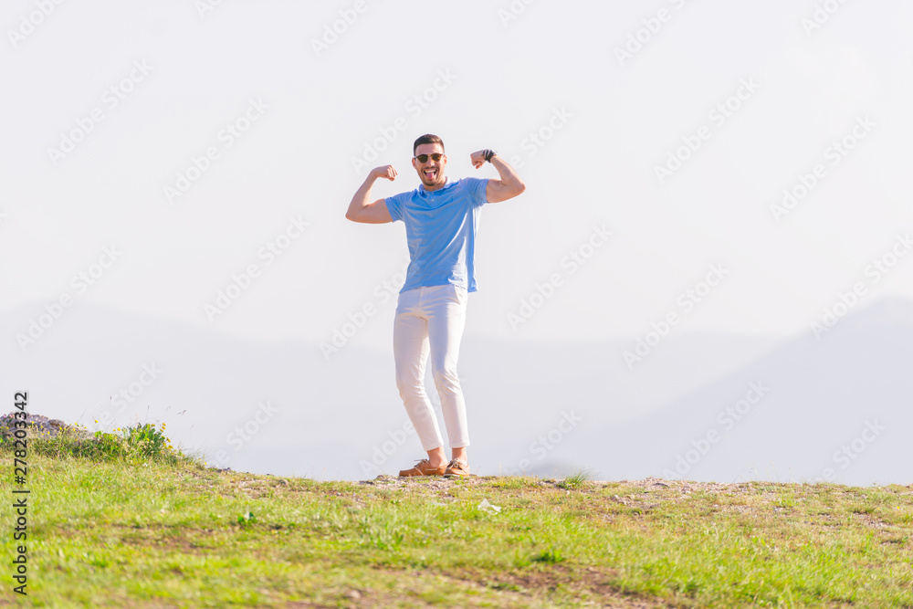 Obraz premium Well dressed ( fashionable) man stands in nature looking over a cliff at the large lake and mountain line while wearing boat shoes, polo shirt and formal pants.