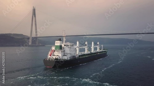 A bulk carrier ship with deck cranes on the sunset time. Cargo ship sailing from open sea. Aerial, high angle, tracking shot