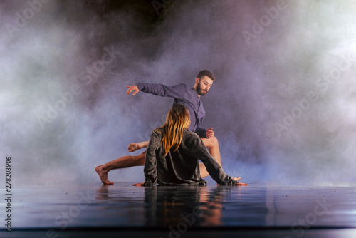 Shoeless dance couple performing multiple unique dance moves in front of a black background surrounded by a lot of smoke.