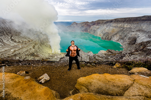 A young man is having fun around in the crater of a volcano against the background of a green sulfur lake and volcanic smoke. photo