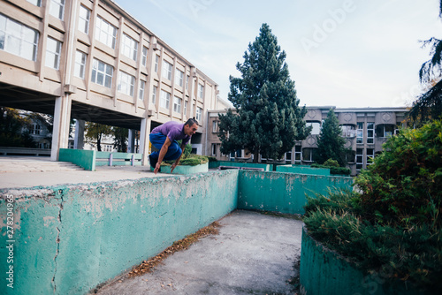 Strongman while training parkour jumping over the concrete wall at an urban area. © qunica.com