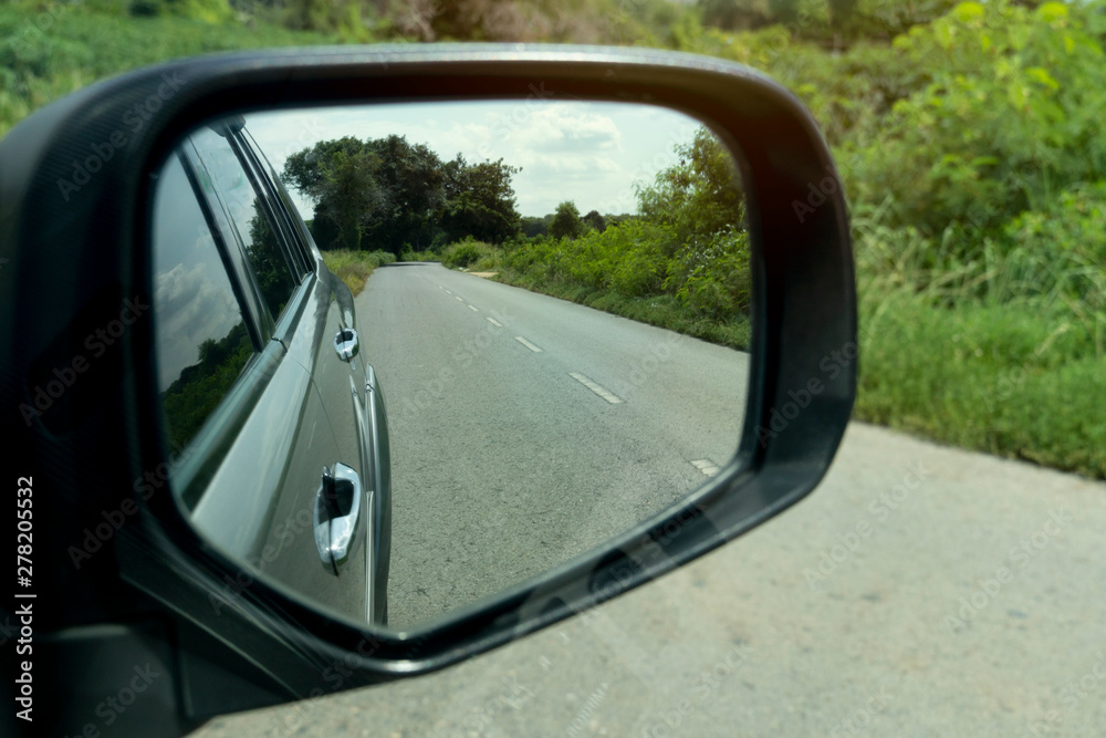 Inside of mirror view of gray car with Asphalt road and green nature.