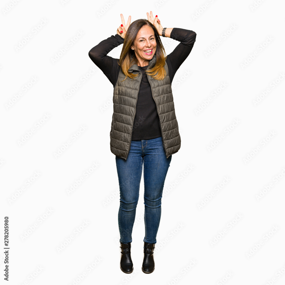 Beautiful middle age woman wearing winter vest Posing funny and crazy with fingers on head as bunny ears, smiling cheerful Beautiful middle age woman wearing winter vest Posing funny and crazy with fingers on head as bunny ears, smiling cheerful