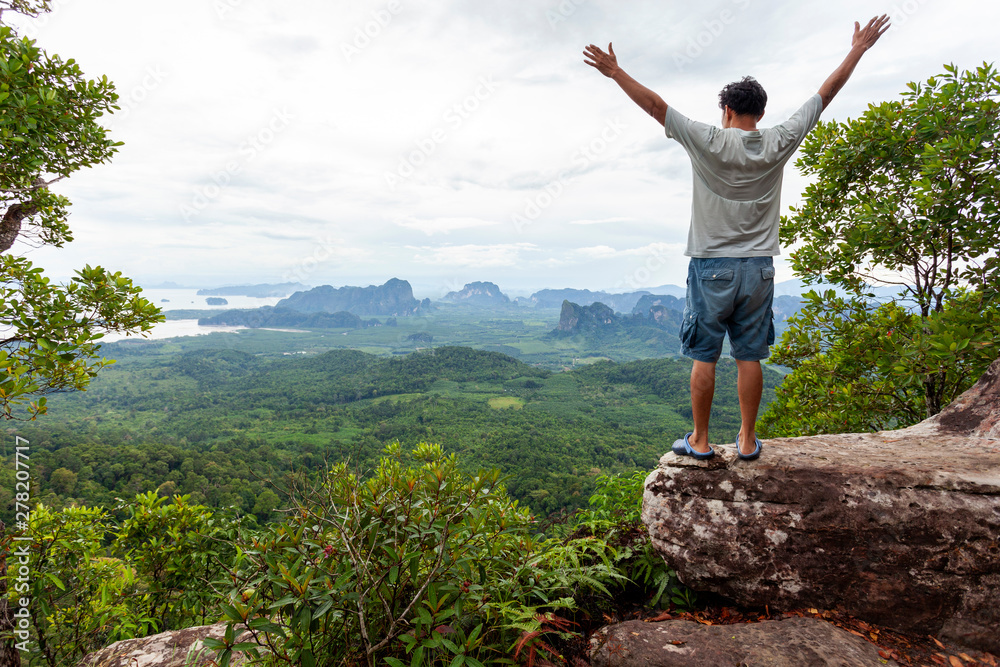 Traveler man standing on big stone holding his hand up and see landscape view at Dragon Crest mountain, popular landmark travel adventure in krabi thailand Traveler man standing on big stone holding his hand up and see landscape view at Dragon Crest mountain, popular landmark travel adventure in krabi thailand
