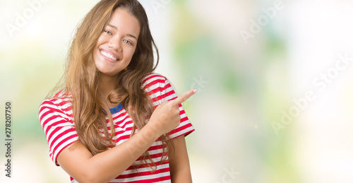 Young beautiful brunette woman wearing stripes t-shirt over isolated background cheerful with a smile of face pointing with hand and finger up to the side with happy and natural expression on face